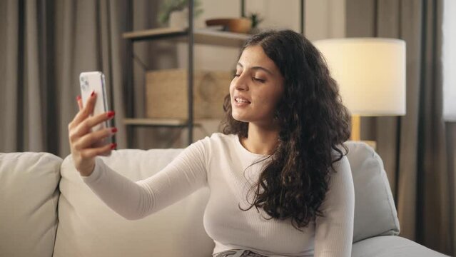 Portrait of beautiful young woman having video call conference meeting interview by smartphone at home Confident curly female talking on pleasant conversation having distance remote relationships