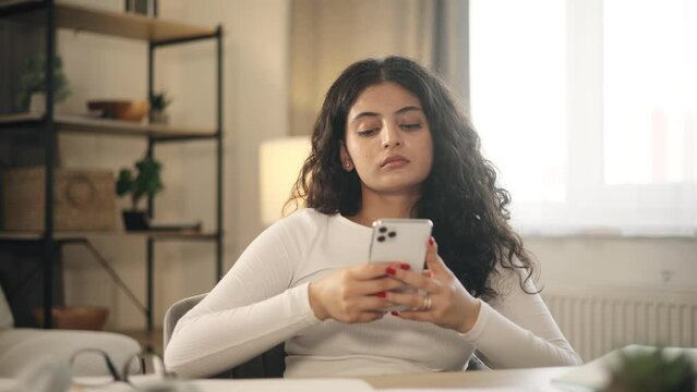 Boring exhausted young woman student or freelancer scrolling feed of social networks products in internet store on smartphone instead of work or education at home workplace Procrastination concept