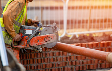 Groundworker builder cutting plastic foul drainage pipe using a petrol-powered saw close-up