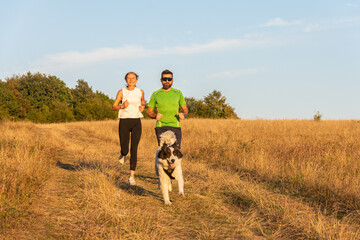 fitness  sport  people and lifestyle concept - happy couple with dog running outdoors