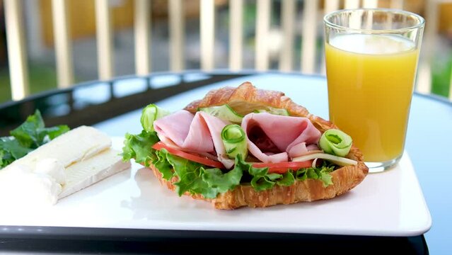 croissant with balyk and cucumber Lettuce leaves tomato delicious breakfast with cheese and orange juice on white plate bacon layers in sandwich on the balcony. delicious food lunch snack
