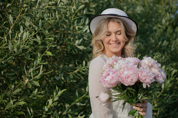 Happy lovely woman florist with bouquet of d peonies on background of green plants in nature. 