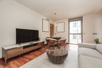 Living room and dining room with a small round wooden table, surrounded by leather and wooden armchairs and glassware on the table, matching coffee table and long sideboard with white marble top