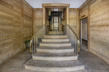 Access portal to the building with brown marble floors on the walls, stairs with golden metal...