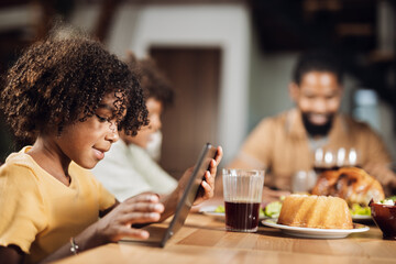 Small African American girl watching something on touchpad at dining table