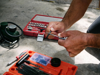 Automobile mechanics. Hands with puncture repair tool kit. Rubber sticky plug, needles and pressurized air compressor.