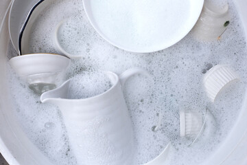 Dishes and bowls in water and bubbles of dishwashing liquid. Kitchen work