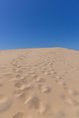 riesige Sanddüne mit Fussabdrücken und blauem Himmel im Hintergrund
