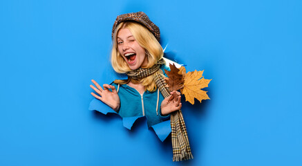 Happy autumn girl wink. Cheerful winking woman in cap and scarf showing ok sign. Winking girl with autumn leaves looking through paper. Autumn fashion collection. Autumn sale. Discount. Advertising. - obrazy, fototapety, plakaty
