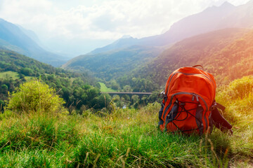 Orange backpack in green grass on top of hill or mountain against amazing view . Travel concept.