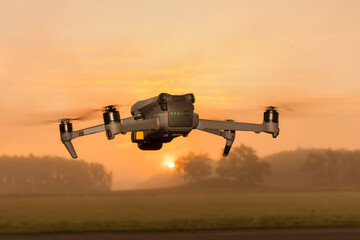 A small foldable drone in flight mode with the spot lights on.. A gray drone in flight in the air. Gray drone in flight in the air. quadrocopter with photo camera flying in the sky.