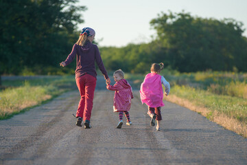 Mother and two children are running along the road countryside. Happy family. - 653453186