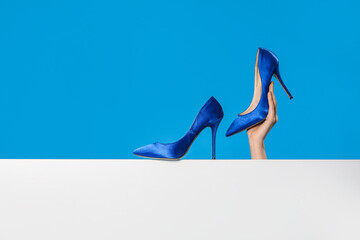 Female hand with elegant high heels on blue background