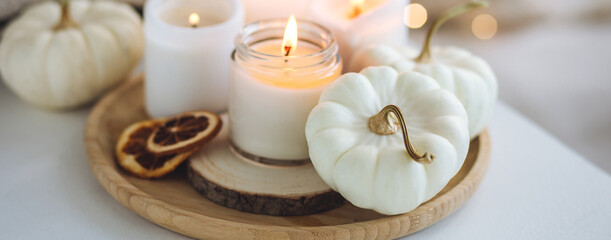 Obraz na płótnie Canvas Atmospheric aroma candles with sweet spicy scent and white pumpkins on wooden tray, autumn bedroom decor. Autumn cozy home and hygge concept, place for relaxation, detention. Aromatherapy. Banner