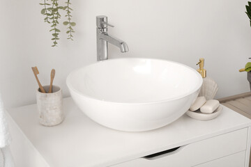 Sink bowl and cup with toothbrushes on chest of drawers in bathroom, closeup