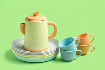 Teapot with cups and plates for baby on green background