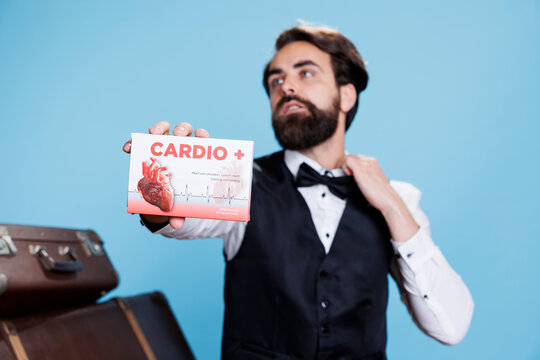 Hotel concierge presents cardiac pills in front of studio camera, recommending medication for heart disease or problems. Young man doorkeeper shows box of medicaments treatment.