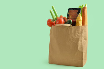 Paper bag with food on green background. Grocery shopping concept