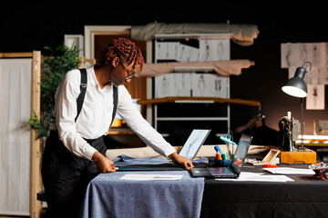 Precise dressmaker meticulously measuring bespoken suit blazer using tape. Seamstress surrounded by...