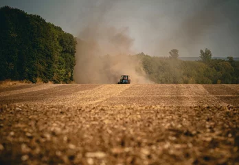 Fotobehang Red tractor sowing in a dusty field © Valerii