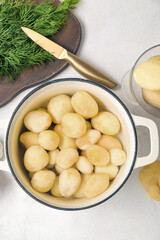 Pot with peeled potatoes on light background