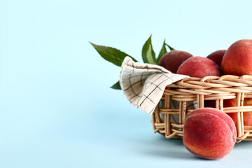 Wicker bowl with sweet peaches and leaves on blue background