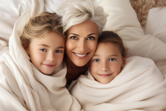 Woman is seen with two children, all wrapped up in warm blankets. This image can be used to depict cozy family moment or importance of staying warm during cold weather