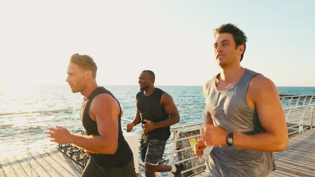 Athletic men jogging along sea in port city at sunset