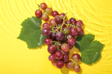 Tasty ripe grapes with leaves in water on yellow background