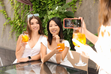 Beautiful young women with glasses of tasty aperol spritz taking photo in cafe, outdoors