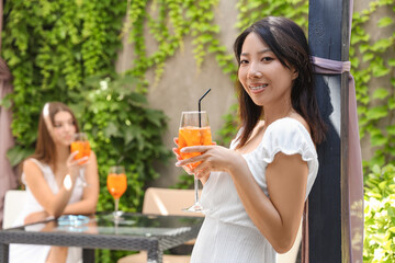 Beautiful young Asian woman with glass of tasty aperol spritz cocktail in cafe, outdoors