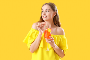 Beautiful young woman with glass of tasty aperol spritz cocktail on yellow background