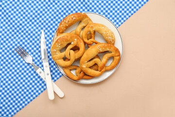 Plate with soft pretzels and cutlery on beige background
