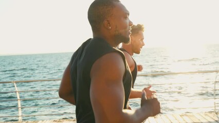 Athletic men jogging along sea in port city at sunset