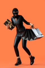 Young woman in balaclava with gift and shopping bags on orange background. Black Friday sale
