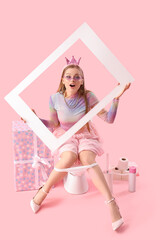Surprised young woman with frame sitting on toilet bowl against pink background