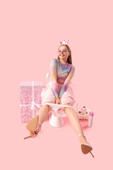 Young woman sitting on toilet bowl and birthday gift against pink background