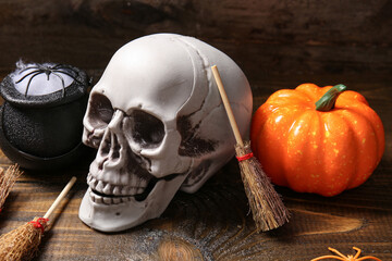Halloween composition with skull, brooms, pumpkin and cauldron on brown wooden background