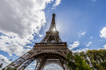Eiffel Tower Paris France with sun starburst, looking up, clouds blue