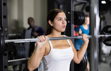 Fototapeta premium Caucasian woman training with barbell using squat rack in gym