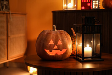 Halloween pumpkins with burning candle on table in dark living room, closeup