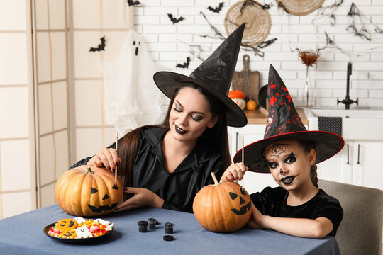 Little girl with her mother painting Halloween pumpkins in kitchen