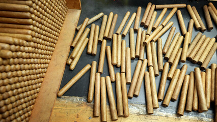 Many just rolled unlabeled handmade cigars are laid in a stack and randomly scattered on a wooden table. The factory for the production of the best cigars in the world