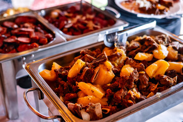 a stainless steel buffet tray with meat and manioc inside