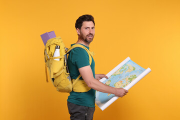 Happy man with backpack and map on orange background. Active tourism