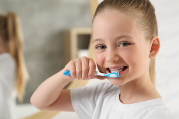 Cute little girl brushing her teeth with plastic toothbrush in bathroom, space for text