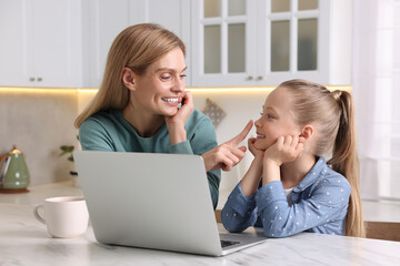 Happy woman and her daughter with laptop at white table indoors - obrazy, fototapety, plakaty