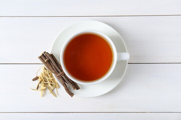 Fototapeta na wymiar Aromatic licorice tea in cup and dried sticks of licorice root on white wooden table, top view