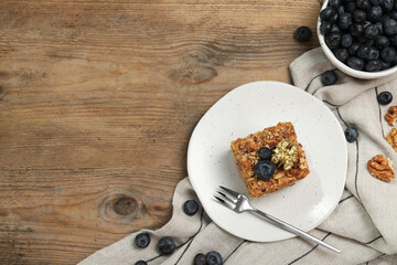 Piece of delicious layered honey cake with blueberries and nuts served on wooden table, flat lay. Space for text