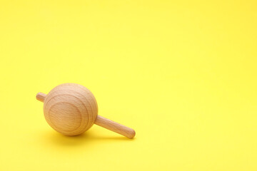 One wooden spinning top on yellow background, space for text. Toy whirligig